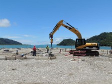 Ram Jack installing helical piles in sandy waterfront area